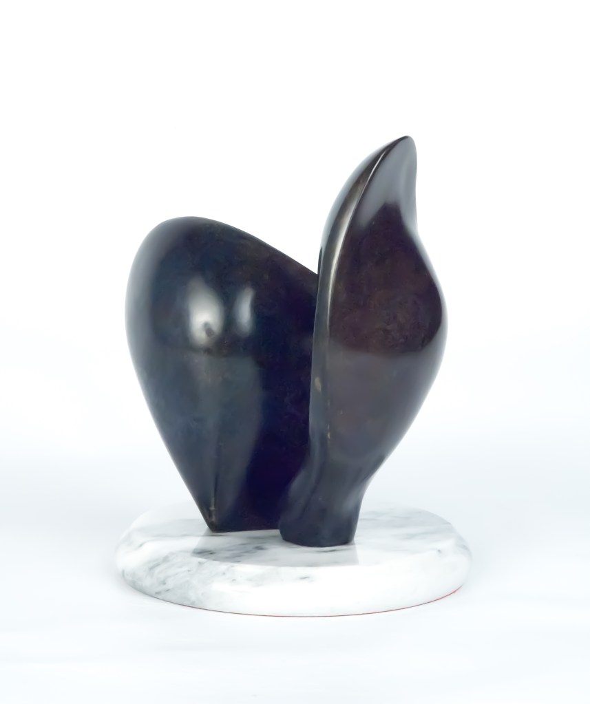Sculpture abstraite noire aux formes douces et épurées, posée sur une base circulaire blanche, évoquant un oiseau stylisé ou une présence protectrice.